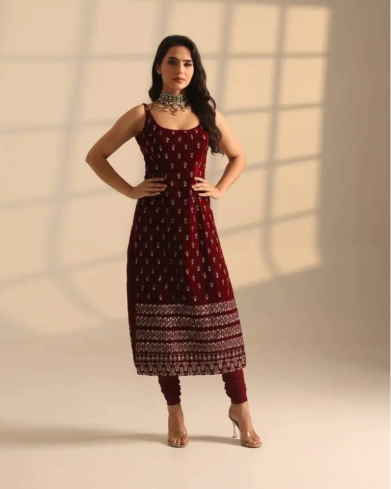 Woman wearing a maroon traditional outfit with a patterned skirt against a neutral background