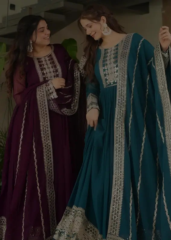 Two women in traditional outfits with intricate designs, one in purple and the other in teal.