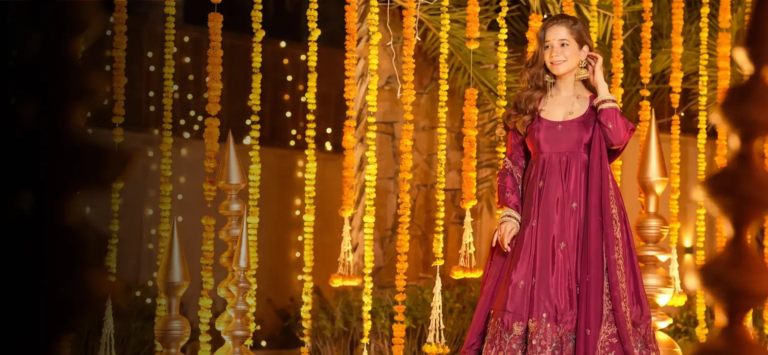 Maroon and gold embroidered Anarkali gown with heavy sequin border, styled in a grand royal corridor setting, luxury couture desktop banner.