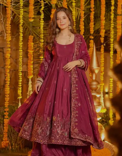 Deep maroon Anarkali dress with gold embroidered dupatta, styled in palace architecture for premium bridal mobile hero image.